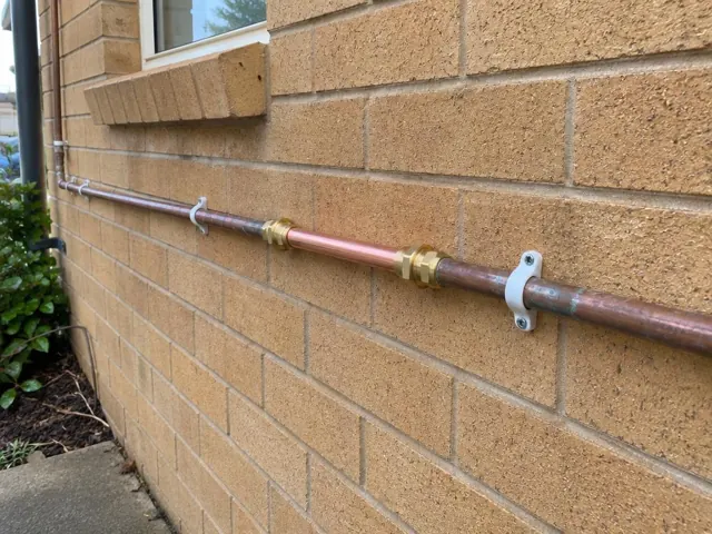 Repaired copper water pipe mounted on a brick exterior wall in Charlestown