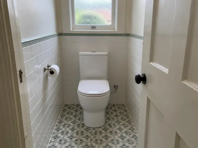 Replaced toilet in a small tiled bathroom with patterned floor and frosted window in Kahibah